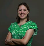Woman in green shirt with crossed arms smiles for a headshot.