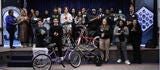 Large group of people standing on a stage around bikes.