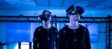 Two men wearing HIVE body suits in a dark room