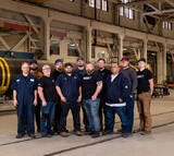 Group photo of Northrop Grumman hydrotesting team standing in a manufacturing facility, with a large solid rocket motor case in the background.
