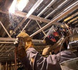 Man with helmet on welding metal with sparks flying.