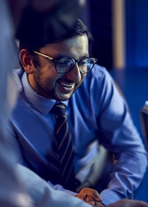 Man in shirt and tie with glasses looking at digital screen.