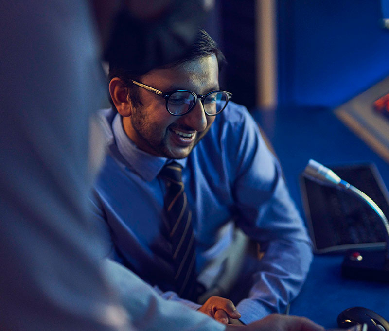 smiling seated man with glasses behind microphone