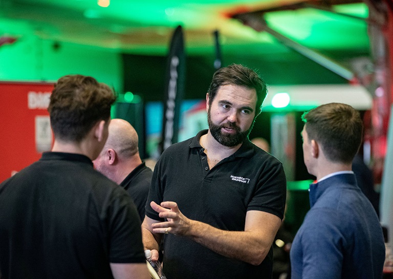 Man with beard in black shirt talking to two other men