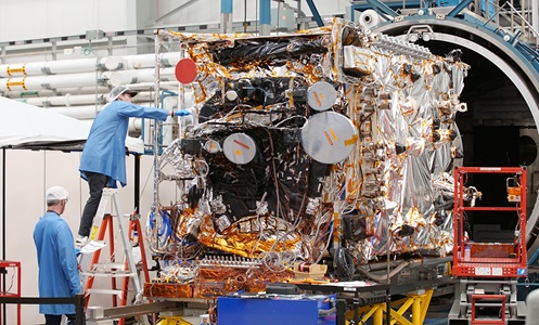 Satellite being worked on by technicians in highbay