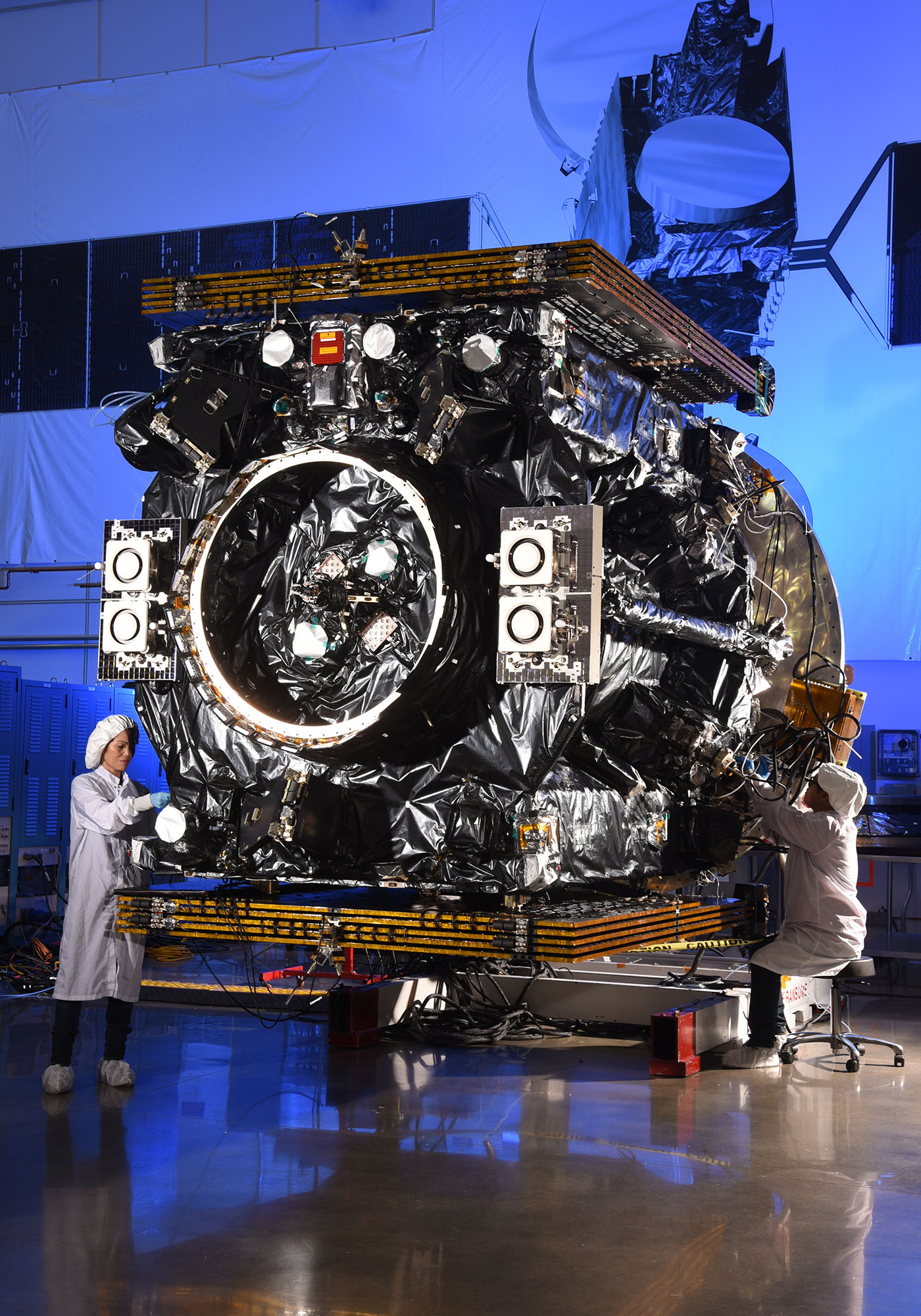 Two engineers assemble the Mission Extension Vehicle spacecraft inside of plant facility