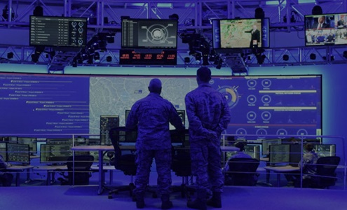 Two men in front of large command control center monitors