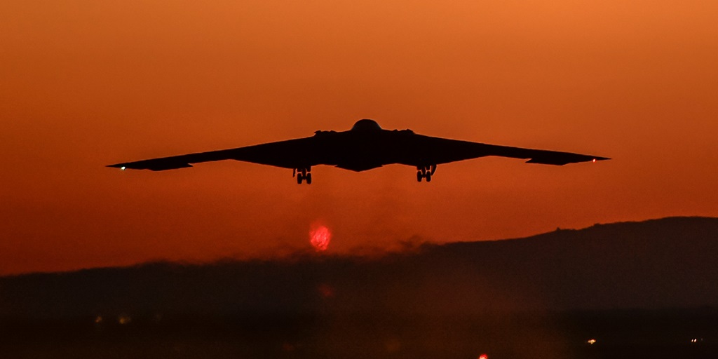 b-2 bomber flying into a red sky at sunset