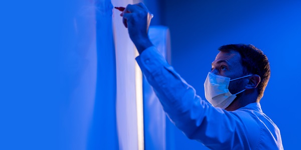 white male wearing mask writing on white board