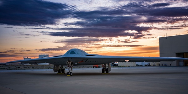 B-21 sitting on tarmac outside hanger at sunset. 