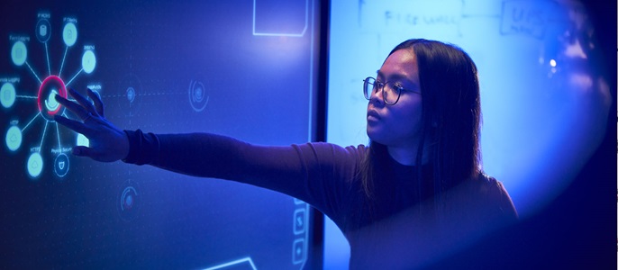 Image of woman touching large digital screen in darkened room. 