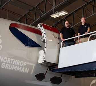 Two men standing outside loading doors for airplane