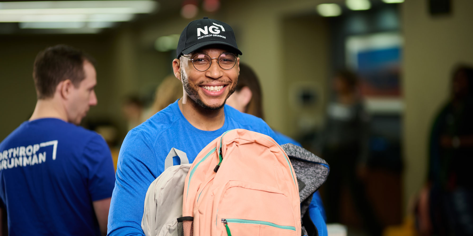 Northrop Grumman employee in branded shirt stands holding a backpack during an event.