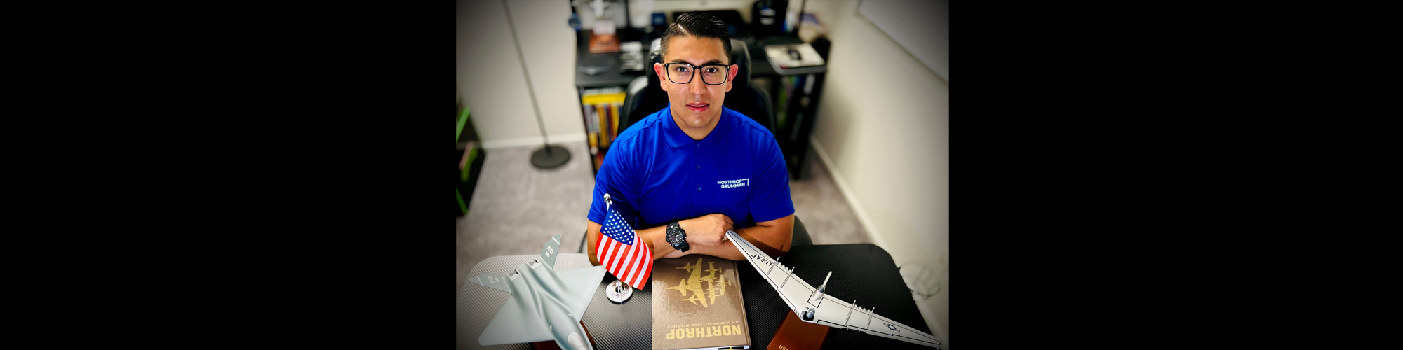 Diego sits at a table with model planes, a Northrop History book and an American flag.
