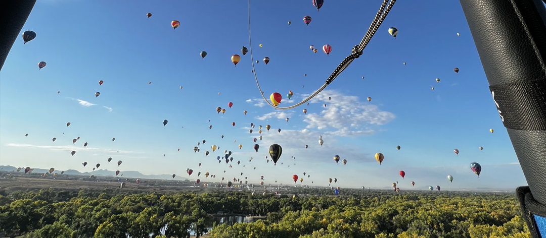 Picture from within hot air balloon showing horizon full of other balloons flying above Earth. 