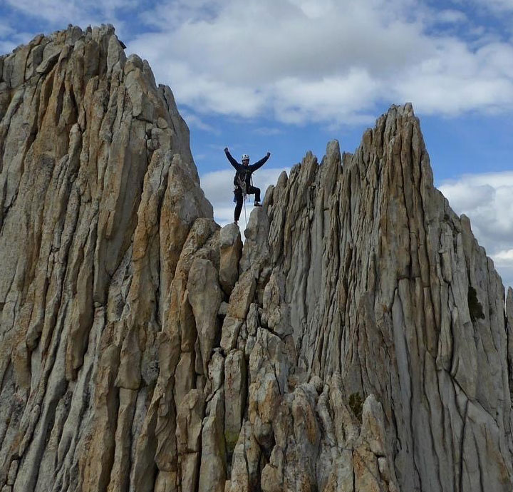 Kia stands on a gray rock structure with his arms outstretched. 