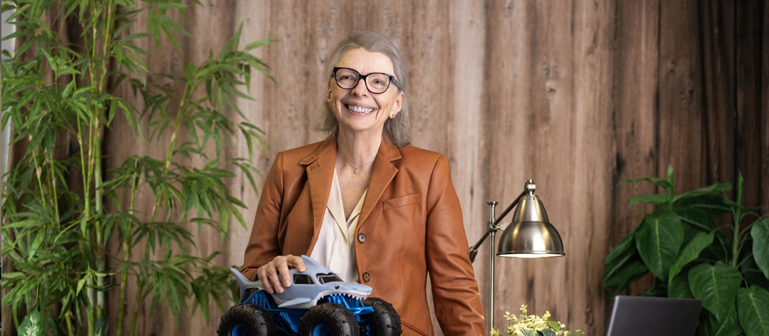 Woman sits on desk with toy truck.