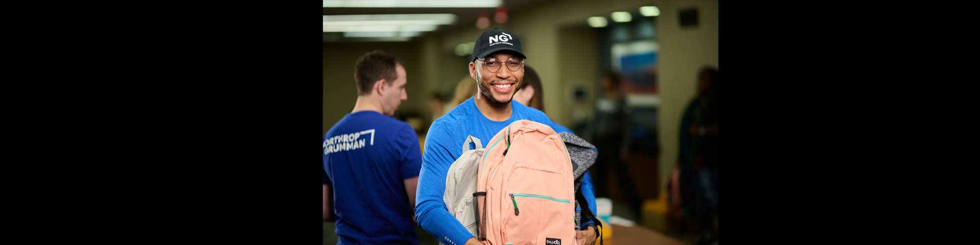 Northrop Grumman employee in branded shirt stands holding a backpack during an event.