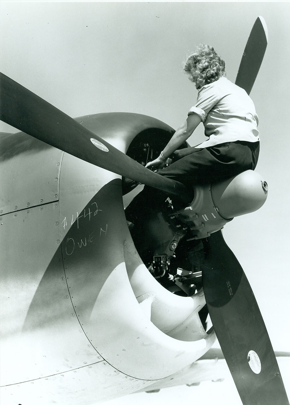 Black and White photo of woman sitting on propeller of world war II plane. 