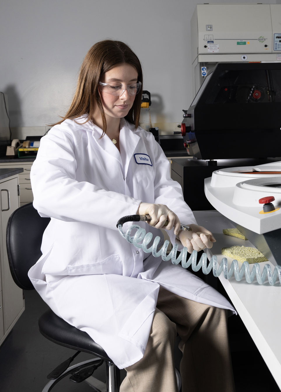 Female engineer in white labcoat sits at desk and works in lab. 