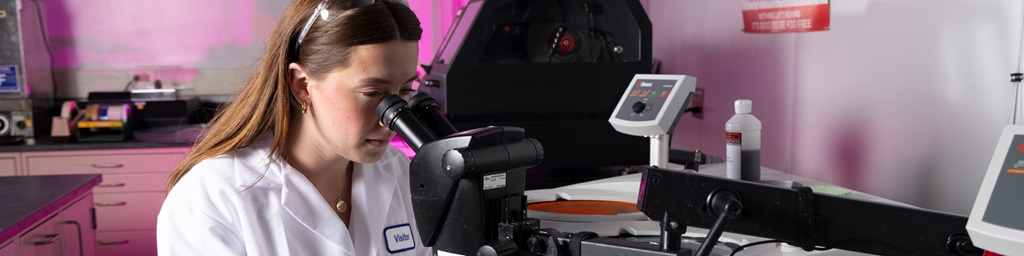 Female engineer in white labcoat sits at desk and works in lab. 