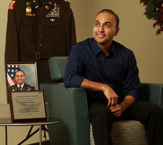 man sitting in chair next to photo and certificate with uniform hanging in background