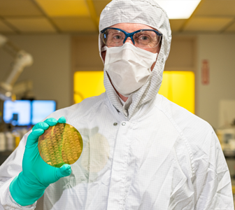 image of man in clean room suit holding a microelectronic wafer.