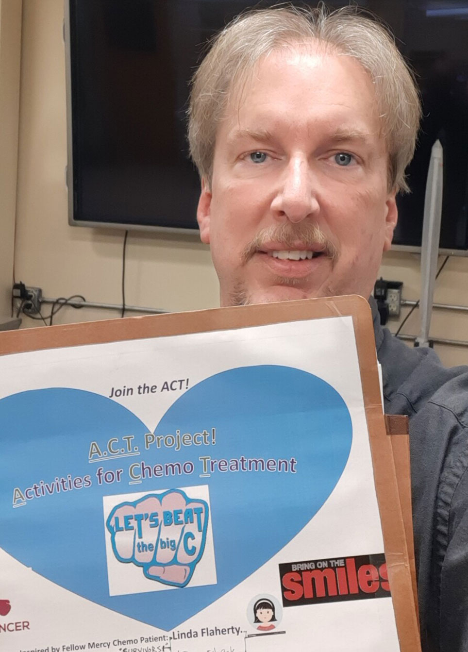 Man in navy shirt holds a folder that reads "A.C.T. Project" Activities for Chemo Treatment."