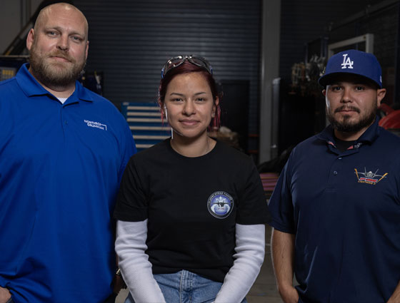 Three employees smiling for a group shot in a machine shop. 