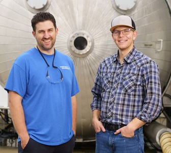 Two rocket motor engineers standing in front of machinery smiling.