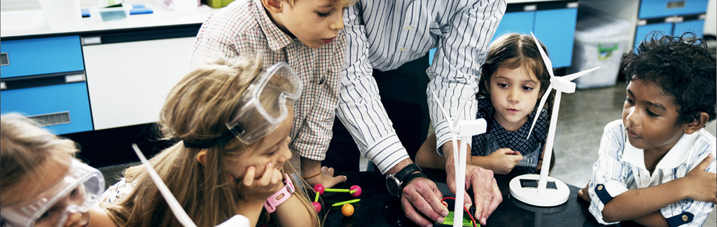 3 girls and two boys observe an adult demonstrating some activity with red wires