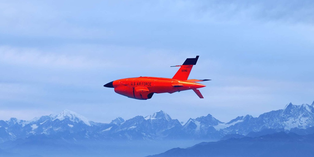 orange aircraft flying against blue sky and mountains in background