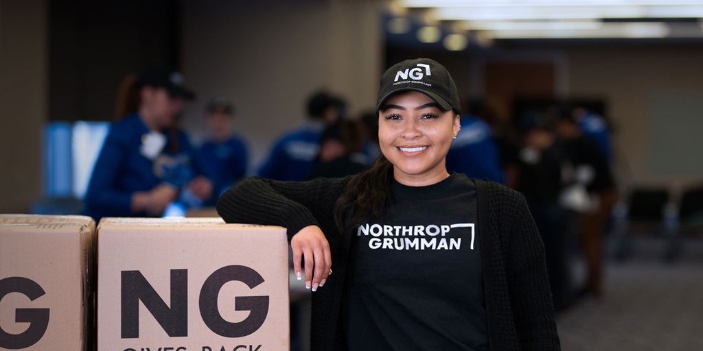 Northrop Grumman employee standing next to cardboard boxes that have the company logo.