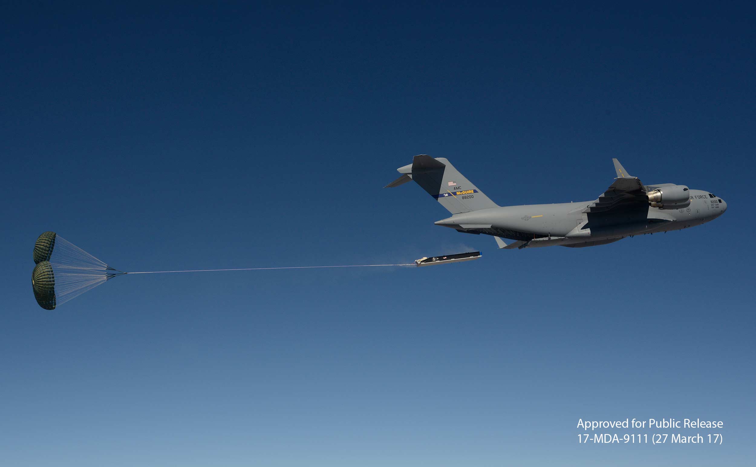 An airdrop load is extracted with parachutes from a C-17 aircraft in air