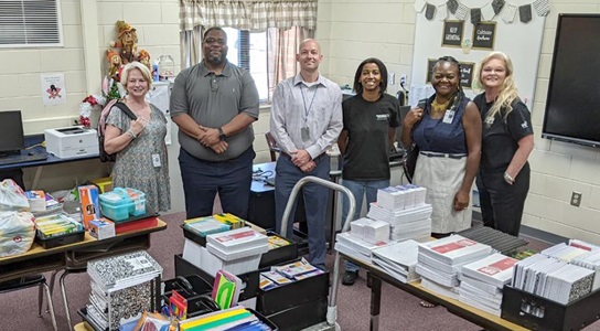 several people lined up in a classroom filled with donations