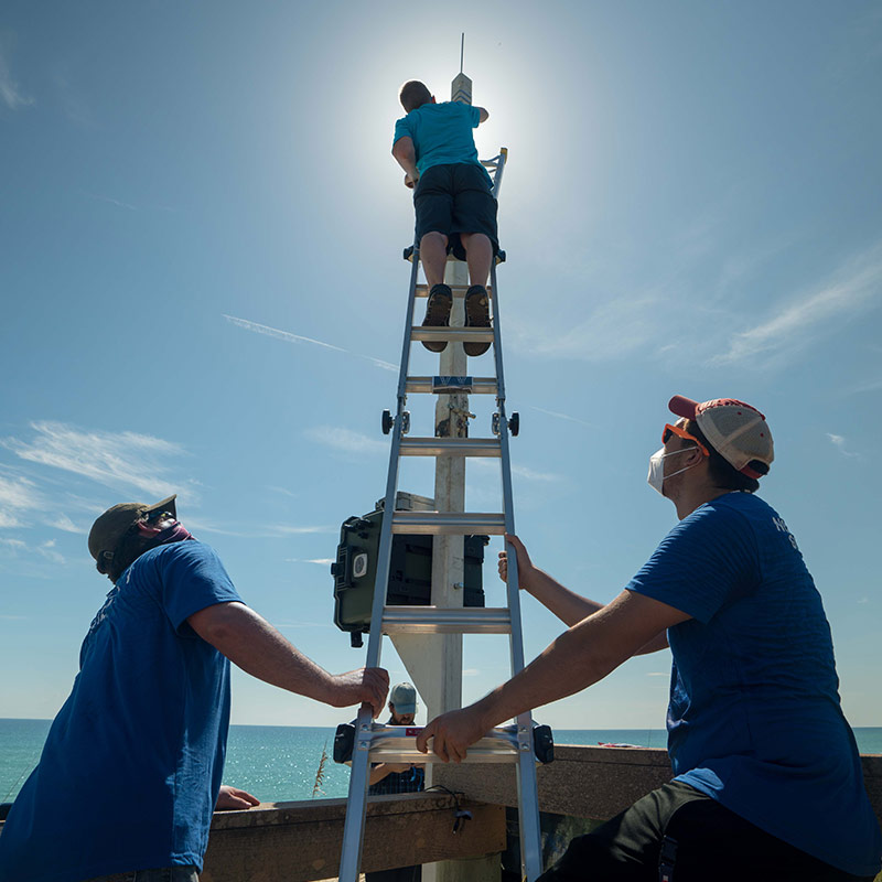 two men holding up ladder for man working at the top