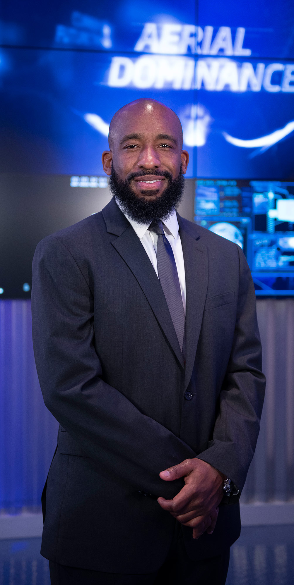 A black man in a suit stands in front of a computerized background