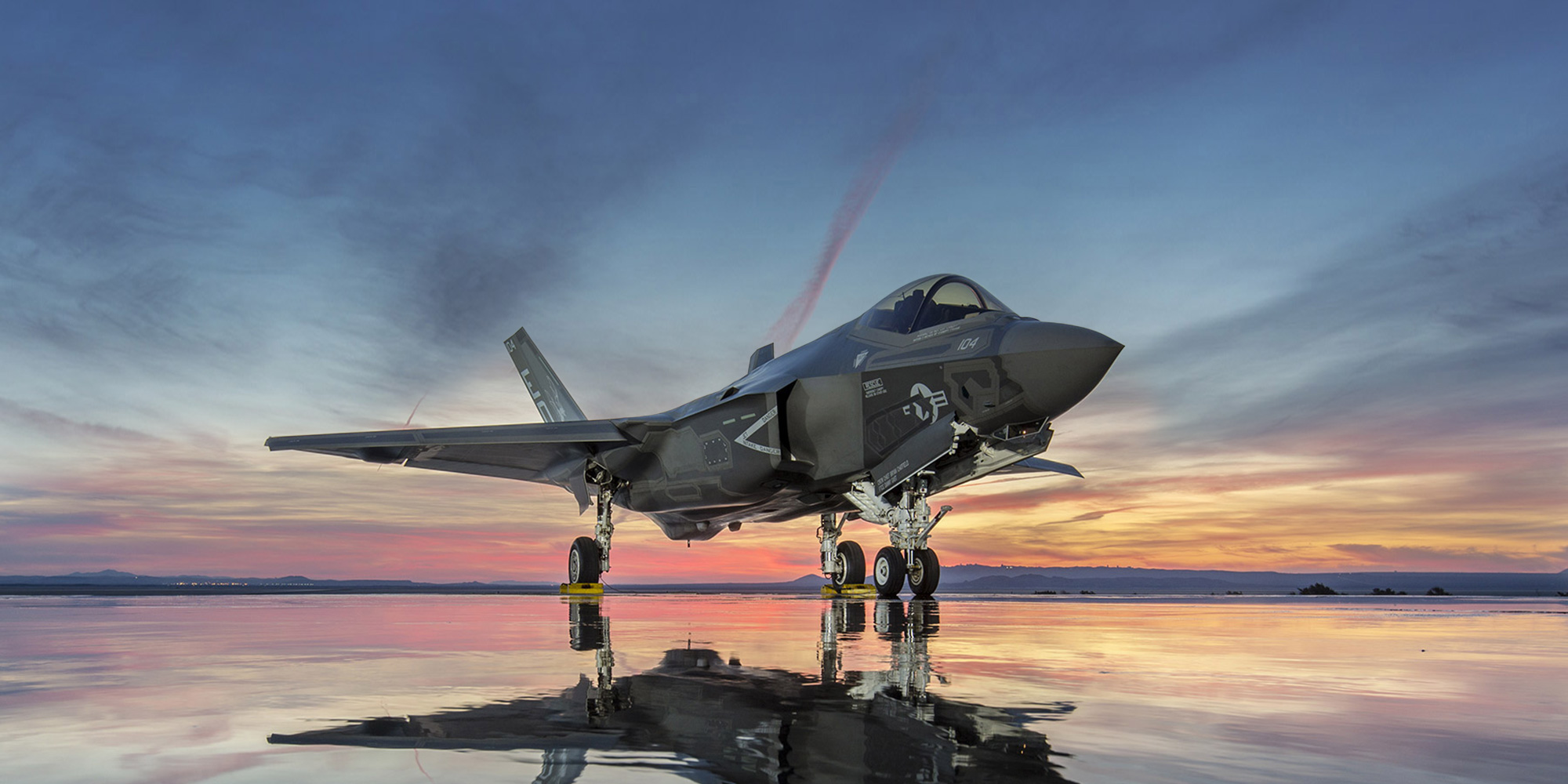 fighter jet at rest on dry lake bed during sunset