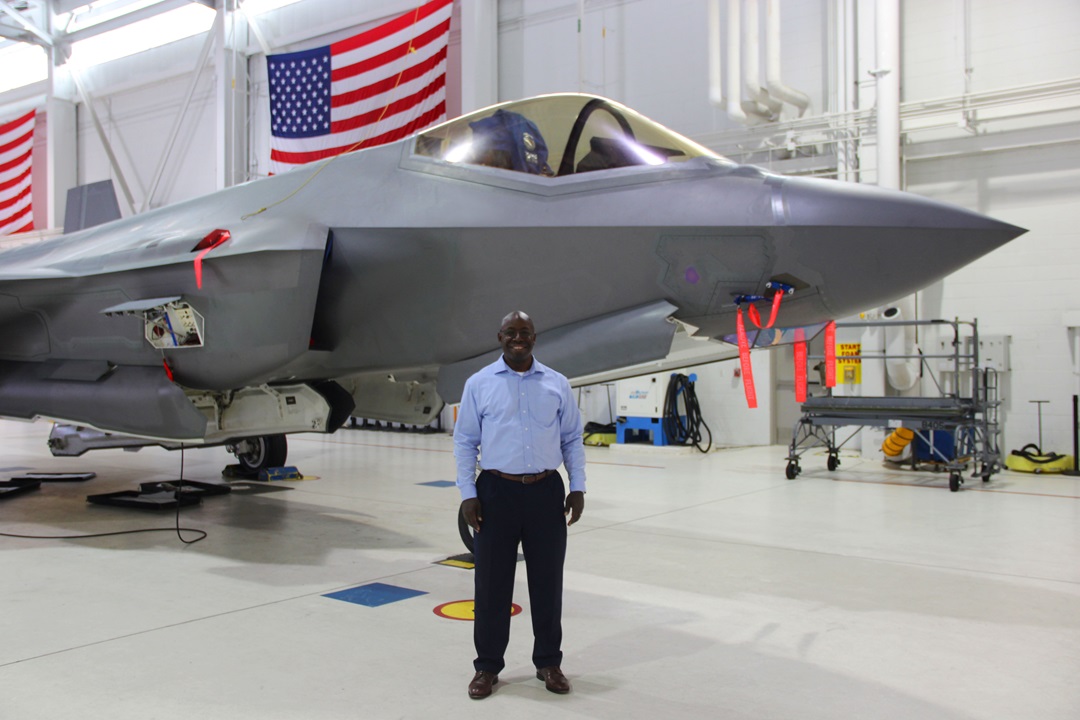 Black man stands smiling in front of aircraft