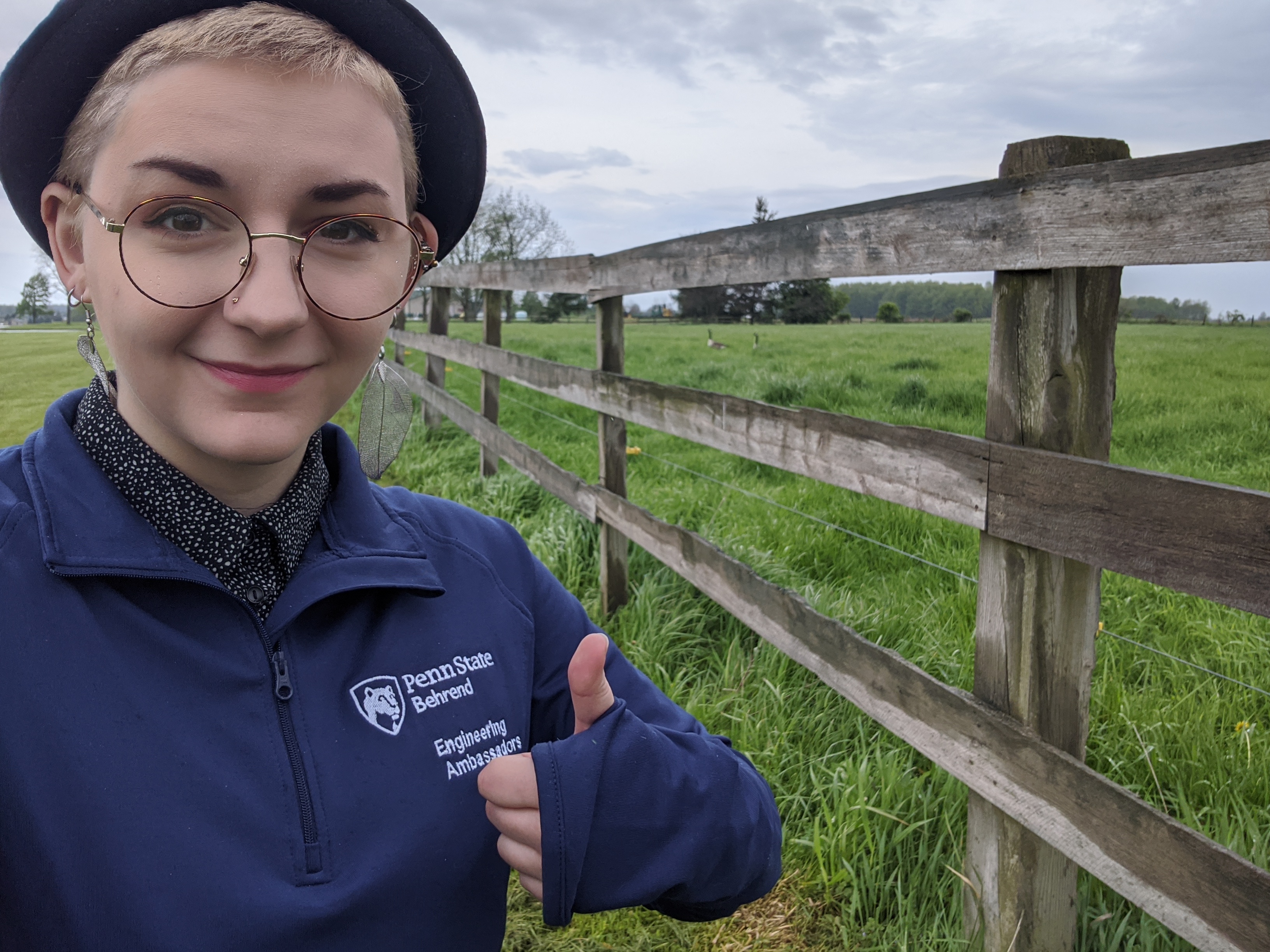 white female intern standing next to wood fence in green field