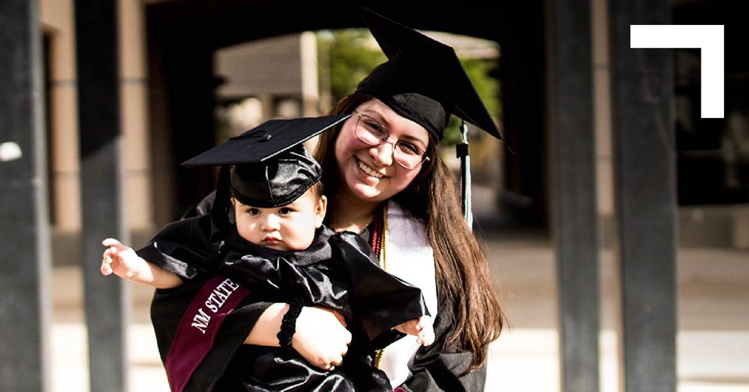 female graduate holding toddler both wearing graduation caps