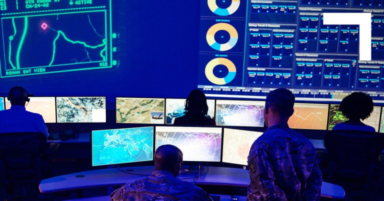 Large command center with multiple computer screens and people monitoring data