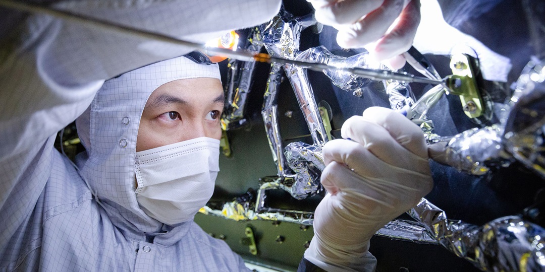 Man in cleanroom suit working on spacecraft