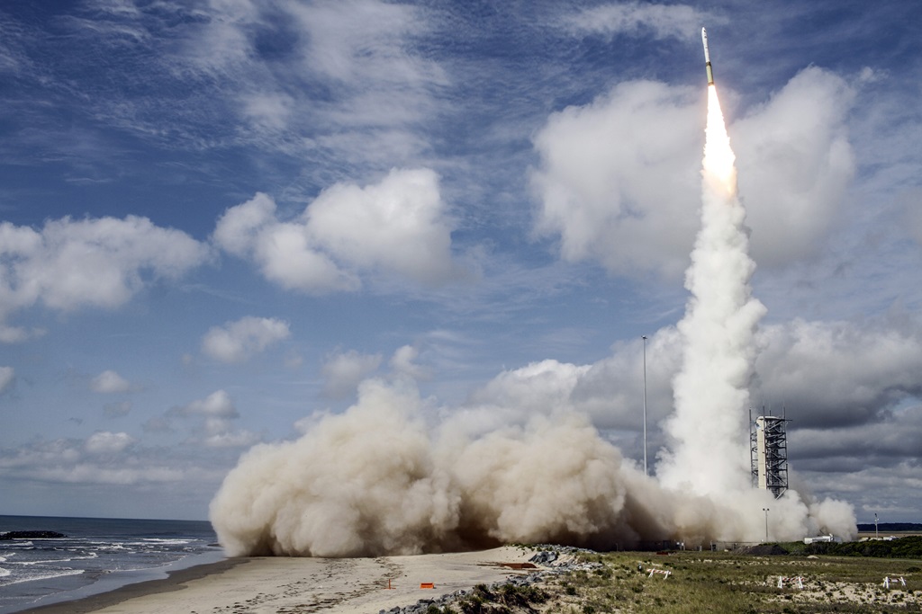 A rocket launching in front of a blue, cloud-filled sky.