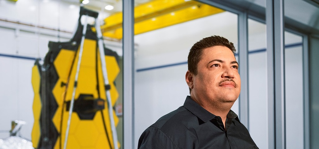 Hispanic man standing in front of James Webb Space Telescope