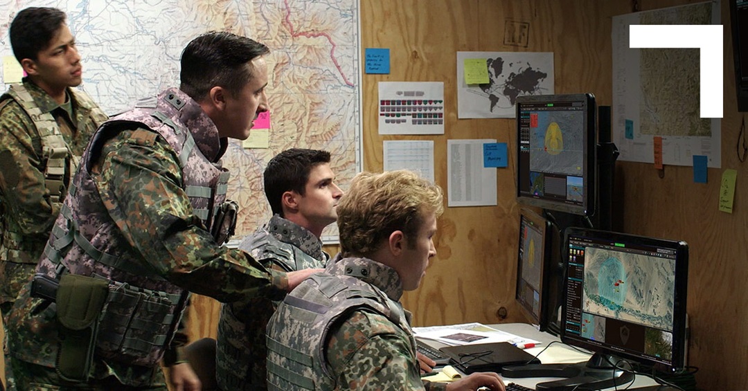 group of people sitting and standing in front of screens with map and paper hanging on the wall