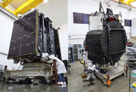 People wear lab coats in manufacturing setting preparing large parts of a spacecraft.