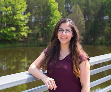 Young woman stands outside smiling in front of lake