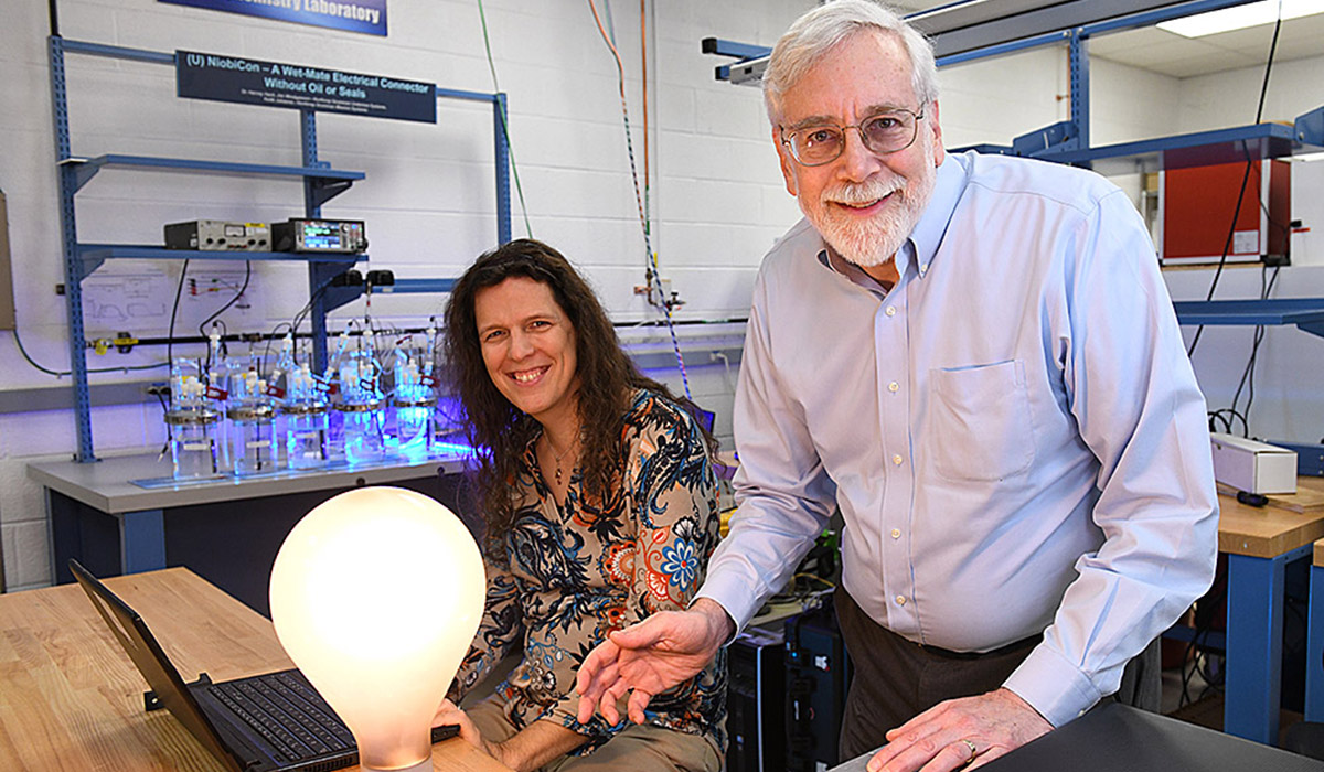 Male and female smiling in front of lightbulb