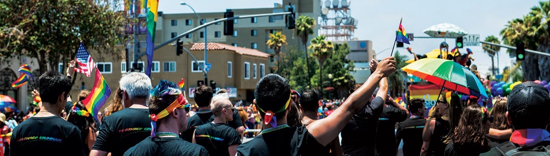 Crowd walking in streets holding rainbow flags and umbrellas